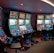 A row of brightly lit slot machines in a casino setting, each with colorful displays and various game themes. The machines are lined up against a dark wall and are unoccupied, with cushioned chairs placed in front of them. The area is dimly lit except for the glow from the screens, creating a vibrant and engaging atmosphere.
